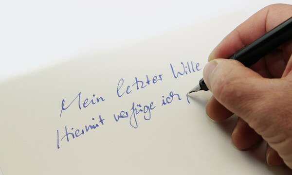 Jemand schreibt mit Füller auf ein Blatt Papier: „Mein letzter Wille. Hiermit verfüge ich, …“