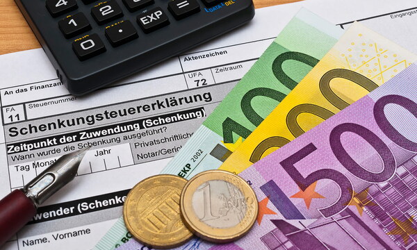 Geldscheine und Münzen liegen auf einer Schenkungssteuererklärung für das Finanzamt