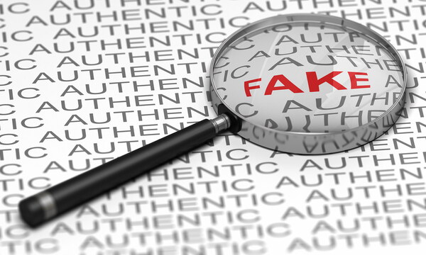 Eine Lupe liegt auf einem Textdokument und fokussiert das rot hervorgehobene Wort „Fake“