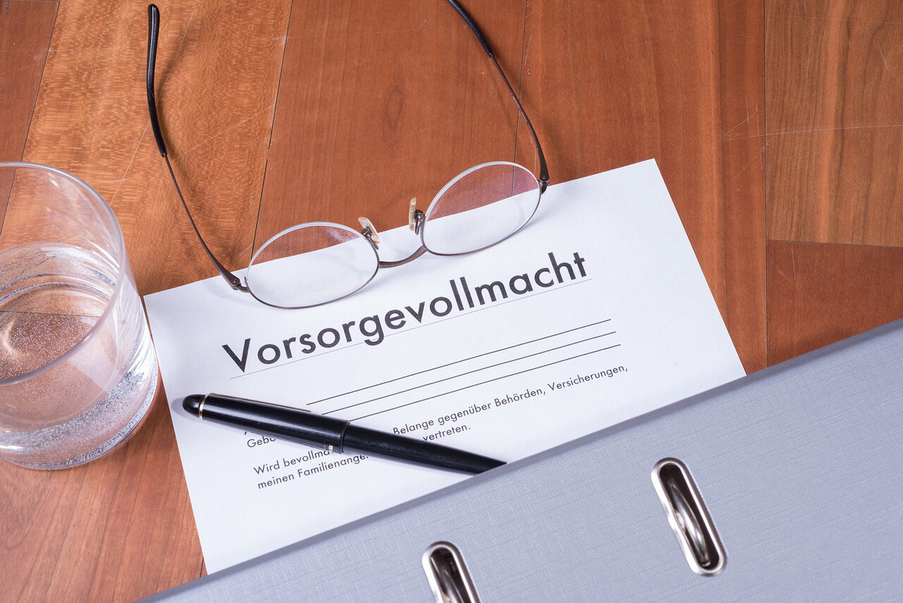 Ein Blatt mit der Überschrift „Vorsorgevollmacht“ liegt auf einem Tisch, darauf liegen eine Brille, ein Kugelschreiber und ein Aktenordner.